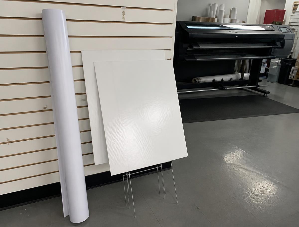 Rolled banner vinyl and blank yard signs beside the wide format printer