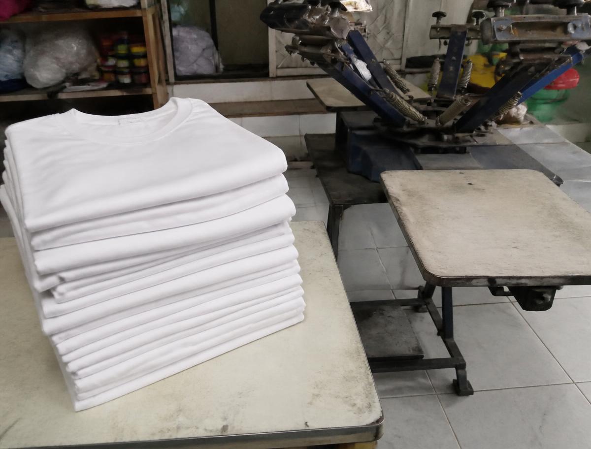 Folded blank cotton t-shirts stacked next to the screen printing press